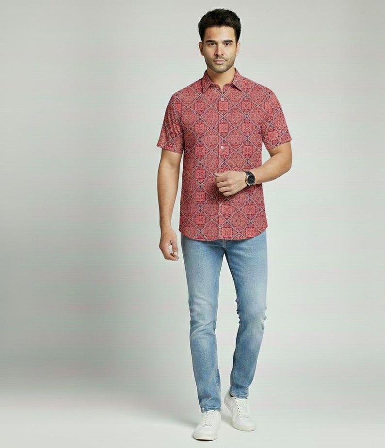 Puede incluir: Una persona con una camisa roja de manga corta con un estampado geom&eacute;trico y vaqueros azul claro. La camisa tiene cuello abotonado y se combina con zapatillas blancas. Se ve un reloj negro en la mu&ntilde;eca.