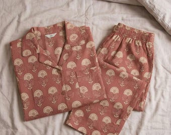 Könnte beinhalten: Ein passendes Schlafanzug-Set in Staubrosa mit floralem Muster. Das Set beinhaltet ein Hemd mit Knöpfen und Brusttasche sowie eine Hose mit elastischem Bund. Das florale Design ist cremefarben.
