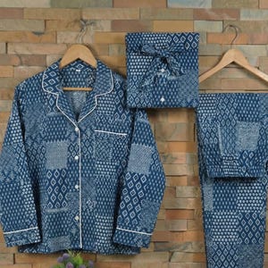 May include: A blue and white patterned pajama set, comprising a button-down shirt, trousers, and a folded set. The pajamas are hanging on wooden hangers. The fabric features a patchwork design with white trim.