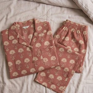 K&ouml;nnte beinhalten: Ein zweiteiliger Schlafanzug in Staubrosa mit floralem Muster. Das Set besteht aus einem Hemd mit Kn&ouml;pfen und einer Brusttasche sowie einer Hose mit elastischem Bund. Das florale Design ist cremefarben.