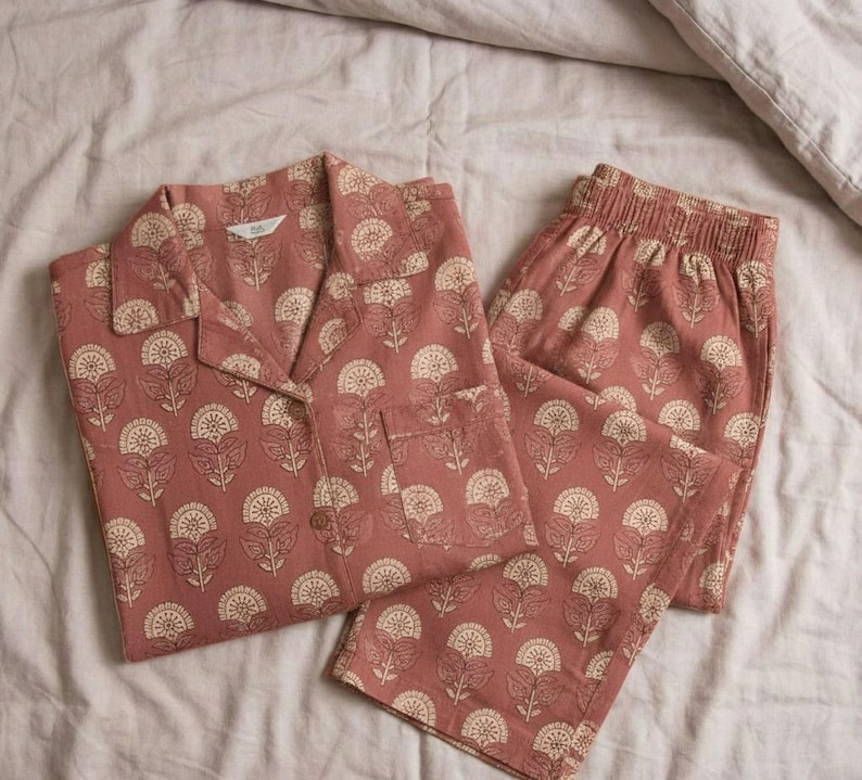 K&ouml;nnte beinhalten: Ein zweiteiliger Schlafanzug in Staubrosa mit floralem Muster. Das Set besteht aus einem Hemd mit Kn&ouml;pfen und einer Brusttasche sowie einer Hose mit elastischem Bund. Das florale Design ist cremefarben.