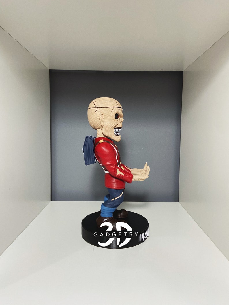 K&ouml;nnte beinhalten: Eine rot-blaue Bobblehead-Figur eines Charakters mit einem sch&auml;delartigen Kopf und einem Rucksack. Die Figur steht auf einem schwarzen Sockel mit dem aufgedruckten Text "3D GADGETRY IRON".