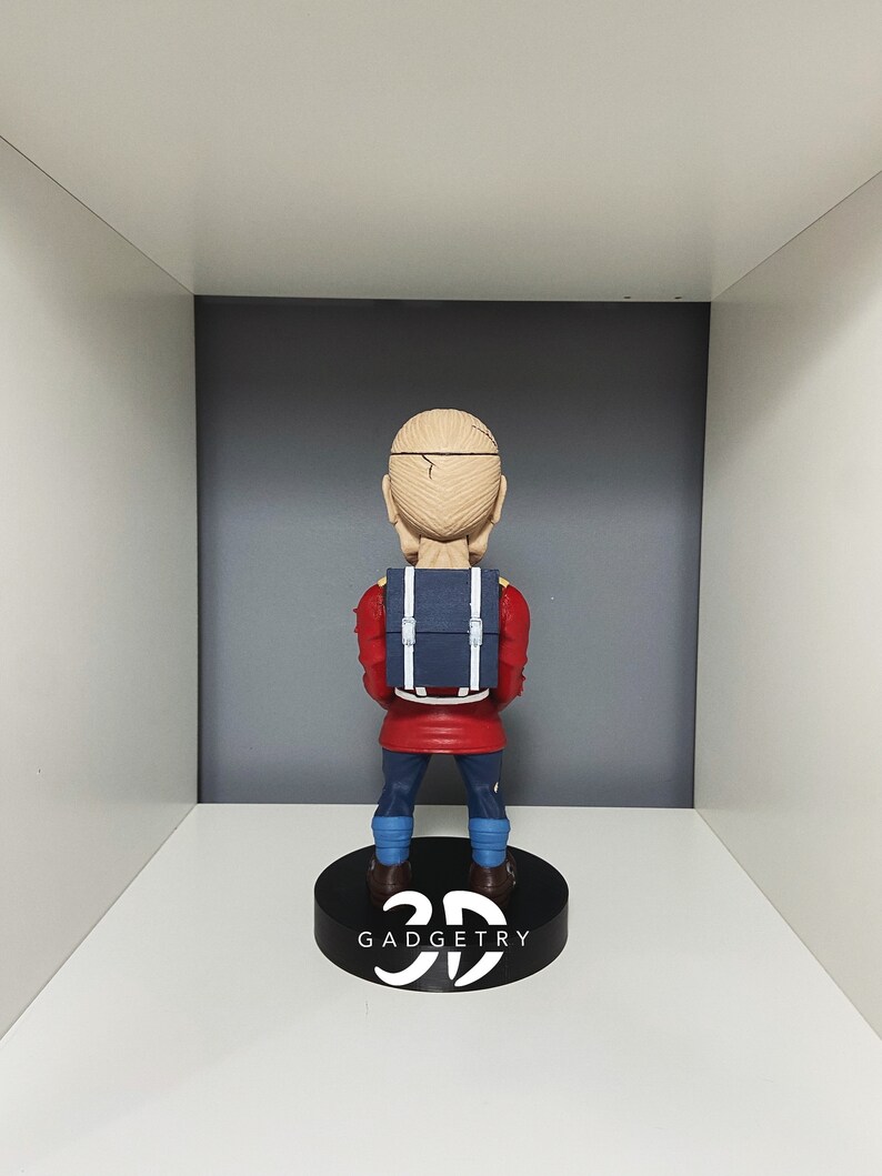 K&ouml;nnte beinhalten: Eine rote und blaue Figur eines Menschen mit einem Rucksack. Die Figur steht auf einem schwarzen Sockel mit dem aufgedruckten Text "3D GADGETRY".