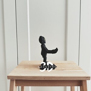 May include: Black figurine of a person with arms outstretched, standing on a wooden base with the text "3D GADGETRY".