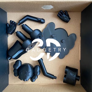 May include: A black 3D printed figure of a cartoon character with a skull and crossbones on its head. The figure is disassembled and comes in multiple pieces, including the head, arms, legs, and a base. The pieces are in a cardboard box.