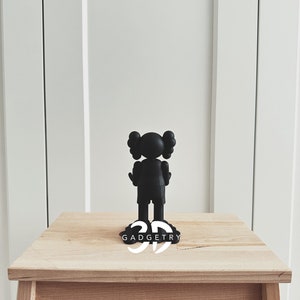 May include: Black figurine of a cartoon character with large ears standing on a wooden table. The figurine is on a black base with the word "GADGETRY" printed in white.