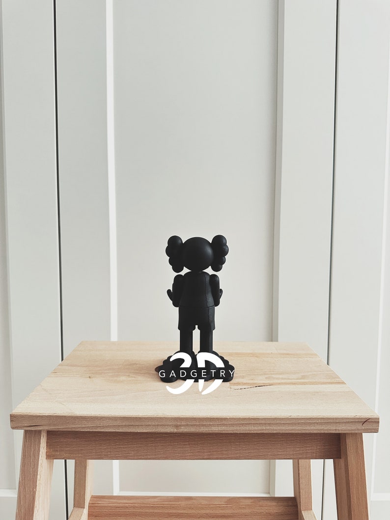 May include: Black figurine of a cartoon character with large ears standing on a wooden table. The figurine is on a black base with the word "GADGETRY" printed in white.