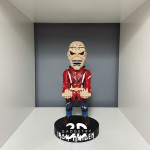 K&ouml;nnte beinhalten: Eine rot-schwarze Bobblehead-Figur eines Mannes mit einem Metallgesicht und einer rot-wei&szlig;en Uniform. Die Figur steht auf einem schwarzen Sockel mit der Aufschrift "3D GadgeTry Iron Maiden".