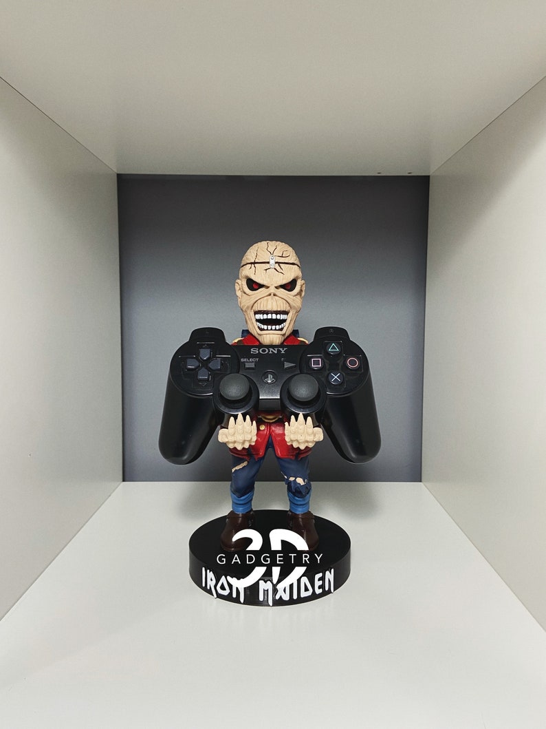K&ouml;nnte beinhalten: Eine schwarze und rote Iron Maiden Figur, die einen schwarzen Sony PlayStation 3 Controller h&auml;lt. Die Figur steht auf einem schwarzen Sockel mit der Aufschrift "3D Gadgetry Iron Maiden".