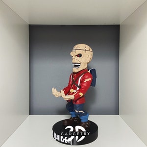 K&ouml;nnte beinhalten: Eine rot-blaue 3D-gedruckte Figur eines Charakters mit einem sch&auml;delartigen Gesicht. Die Figur steht auf einem schwarzen Sockel mit dem aufgedruckten Text "3D GADGETRY" und "MAIDEN".