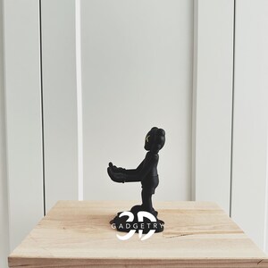 May include: Black figurine of a cartoon character with yellow eyes, standing on a wooden table with the text "3D GADGETRY" printed on the surface.