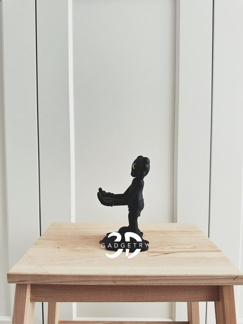 May include: Black figurine of a cartoon character with yellow eyes, standing on a wooden table with the text "3D GADGETRY" printed on the surface.