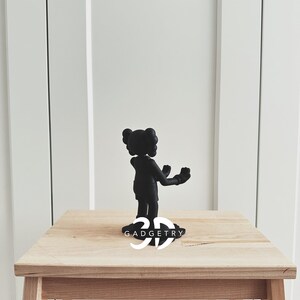May include: Black figurine of a cartoon character with arms outstretched, standing on a wooden table with the text "3D GADGETRY" printed on the surface.