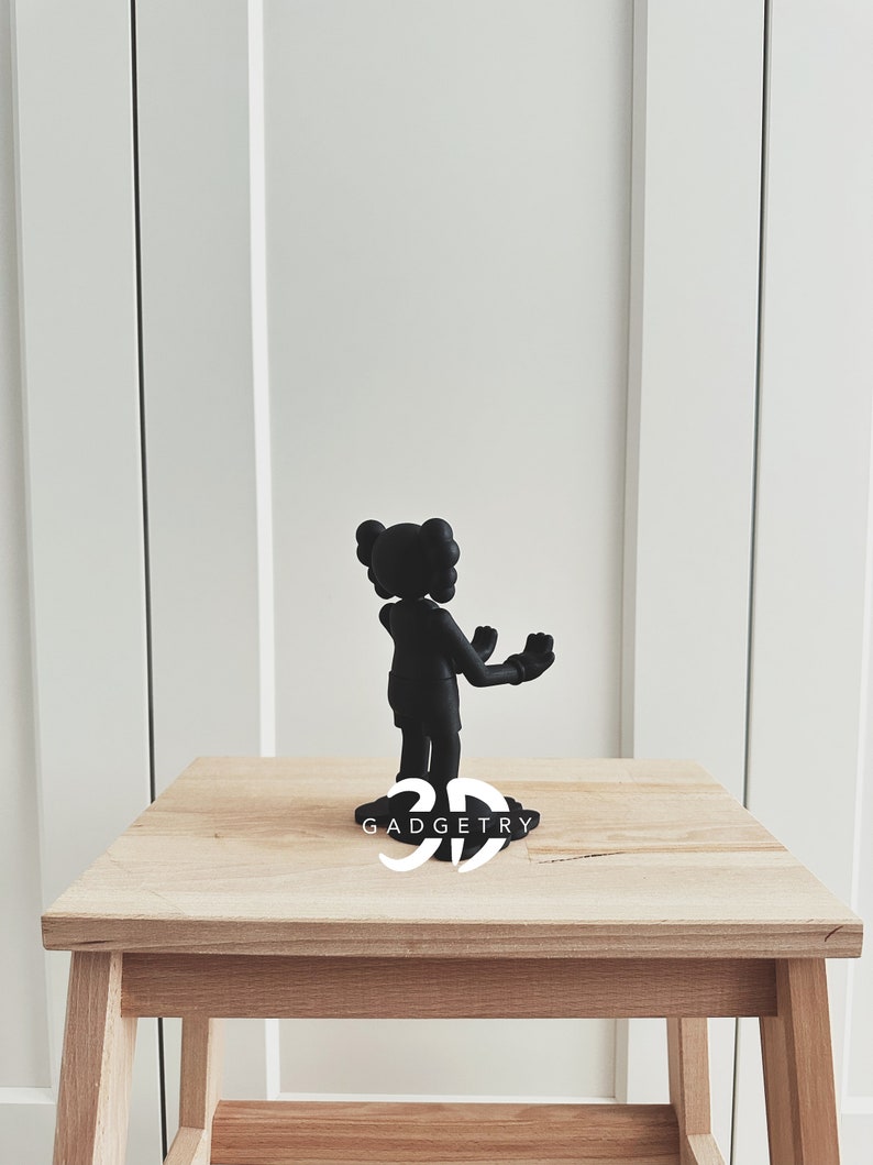 May include: Black figurine of a cartoon character with arms outstretched, standing on a wooden table with the text "3D GADGETRY" printed on the surface.