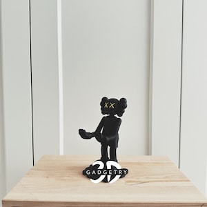 May include: Black and white 3D printed figurine of a character with yellow X's for eyes. The figurine is standing on a black base with the word "GADGETRY" printed in white.
