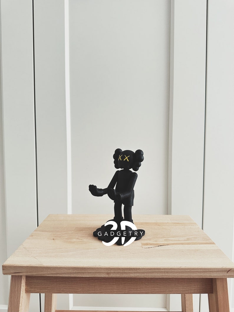 May include: Black and white 3D printed figurine of a character with yellow X's for eyes. The figurine is standing on a black base with the word "GADGETRY" printed in white.