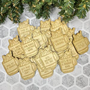 May include: A set of 15 wooden ornaments shaped like mugs of hot chocolate with various Christmas-themed phrases, such as "Let's Watch a Christmas Movie", "Let's Decorate the Tree", and "Let's Read a Holiday Book".