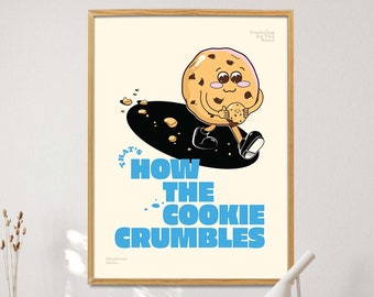 May include: A framed art print featuring a cartoon cookie character with a smaller cookie. The print has the text "THAT'S HOW THE COOKIE CRUMBLES" in blue. The artwork is displayed on a desk with a wooden chair and a lamp.