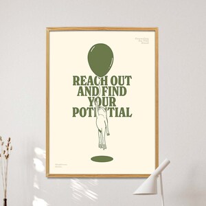 Pu&ograve; includere: Una stampa artistica incorniciata con la scritta "REACH OUT AND FIND YOUR POTENTIAL" in lettere verdi. L'opera presenta un palloncino verde e una figura che si protende verso un cerchio verde. La stampa &egrave; esposta su una scrivania con una sedia di legno.