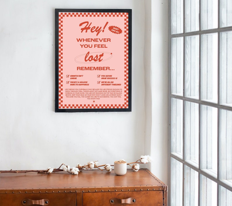 May include: A framed poster with a pink background and red checkered border. The poster features the words "Hey! Whenever you feel lost, remember..." in a retro font. The poster also includes a list of inspirational reminders.