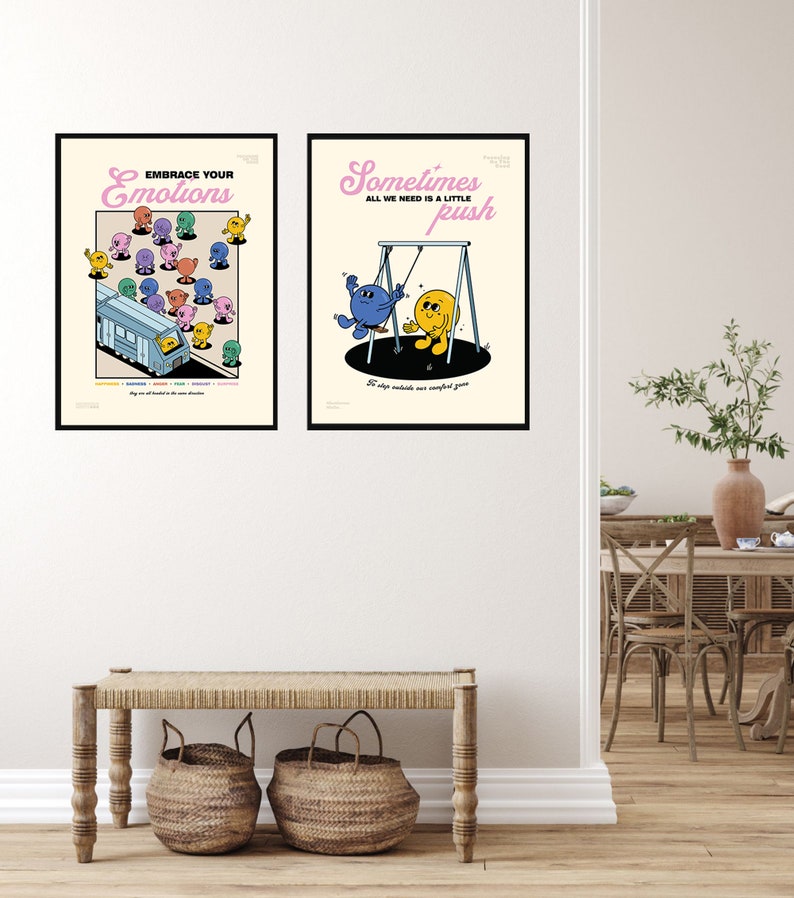 May include: Two framed art prints with black borders hang on a white wall. The left print reads "Embrace Your Emotions" with colorful cartoon characters. The right print says "Sometimes All We Need Is a Little Push" with cartoon figures on a swing.