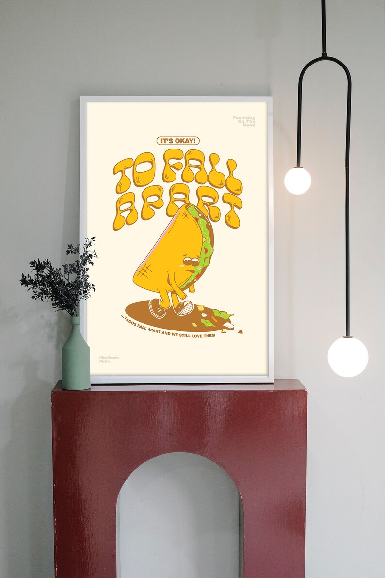 May include: A framed art print featuring a cartoon taco with a sad expression, with the words "TO FALL APART" in large, retro-style lettering. The text "IT'S OKAY!" is above the taco, and "- TACOS FALL APART AND WE STILL LOVE THEM" is below.
