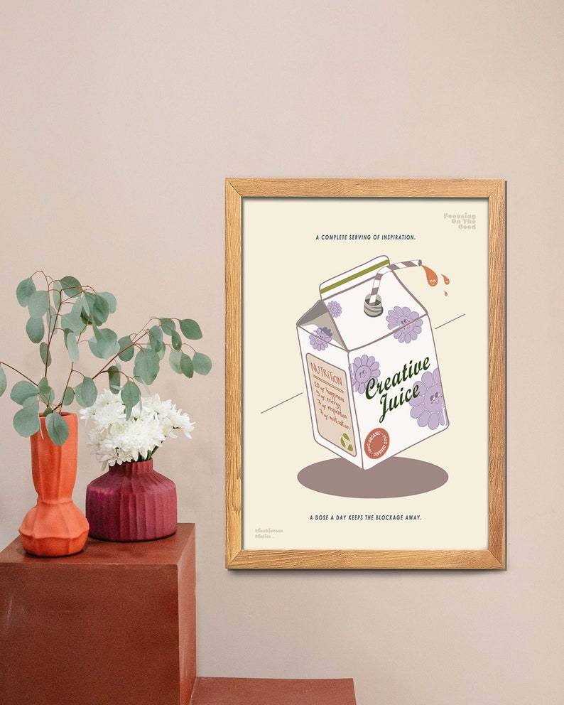 May include: A framed print featuring a cartoon illustration of a Creative Juice carton with a straw, purple flowers, and the text "Creative Juice." The print includes the text "A complete serving of inspiration" and "A dose a day keeps the blockage away."