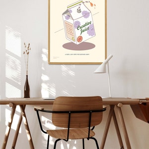 May include: A framed poster featuring a cartoon illustration of a Creative Juice carton with purple flower accents. The poster includes text that reads "A complete serving of inspiration" and "A dose a day keeps the blockage away."