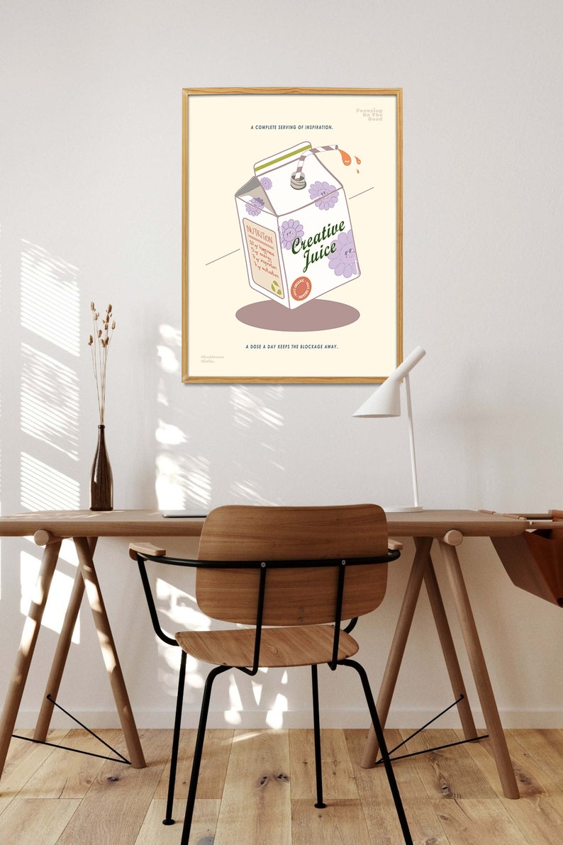 May include: A framed poster featuring a cartoon illustration of a Creative Juice carton with purple flower accents. The poster includes text that reads "A complete serving of inspiration" and "A dose a day keeps the blockage away."