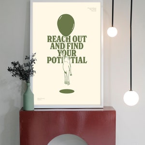 Pu&ograve; includere: Una stampa artistica incorniciata con la scritta "REACH OUT AND FIND YOUR POTENTIAL" in verde oliva. L'immagine presenta una persona che raggiunge un palloncino. La stampa &egrave; esposta su una mensola rossa con un vaso e una pianta verdi.