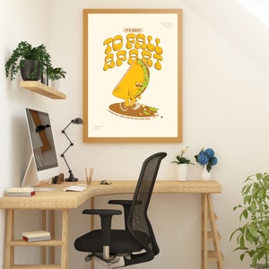 May include: A framed art print with a cartoon taco character that reads "It's Okay To Fall Apart". The taco is yellow and green, with a sad expression. The print is in a light wood frame, displayed in a home office setting.
