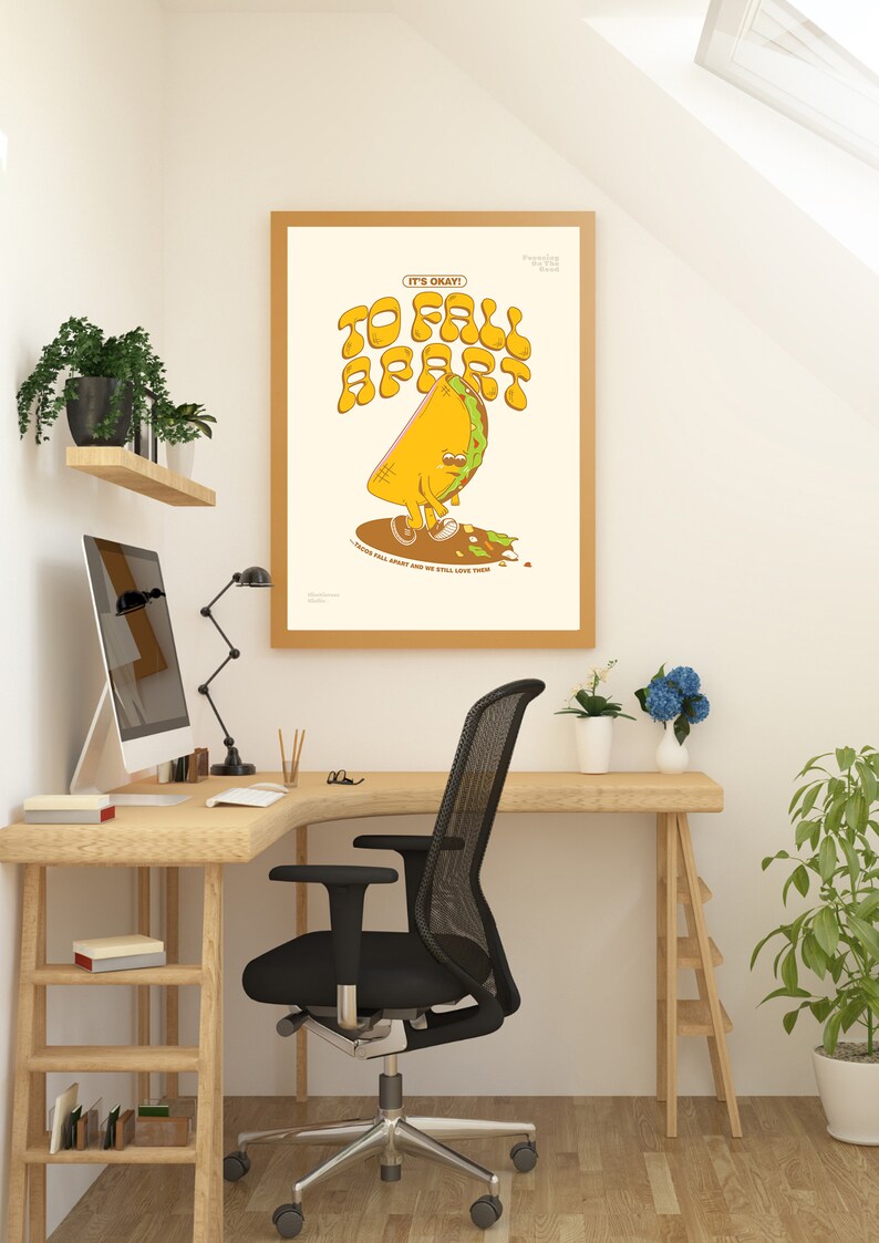 May include: A framed art print with a cartoon taco character that reads "It's Okay To Fall Apart". The taco is yellow and green, with a sad expression. The print is in a light wood frame, displayed in a home office setting.