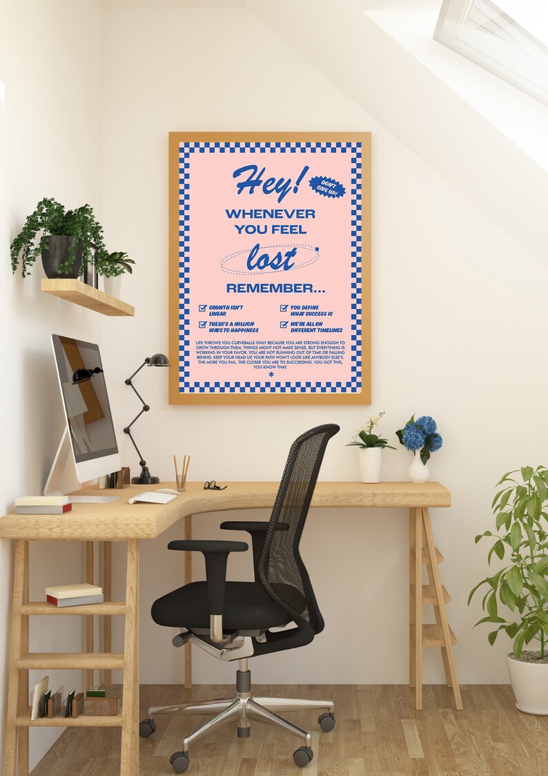 May include: A framed poster with a pink background and blue checkered border. The poster reads "Hey! Whenever you feel lost, remember..." with a list of inspirational reminders. The poster is displayed on a wooden desk with a black office chair.