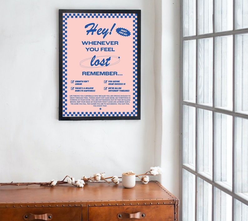 May include: A framed poster with a pink background and blue text. The poster reads "Hey! Whenever you feel lost, remember..." with a list of affirmations. The frame is black with a blue and white checkered border. A motivational art print.