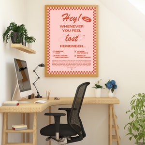 May include: A motivational poster with a pink background and a wooden frame. The poster reads "Hey! Whenever you feel lost, remember..." with a list of reminders. The poster is displayed in a home office setting with a desk, chair, and plants.