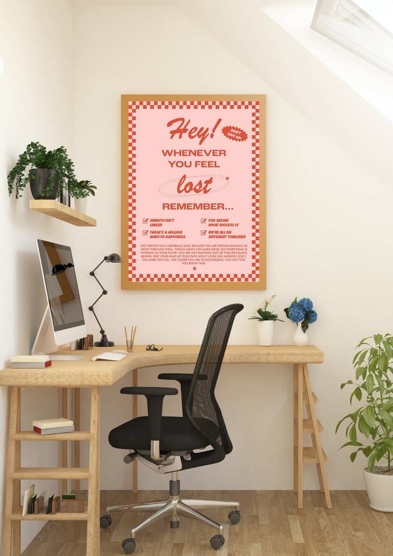 May include: A motivational poster with a pink background and a wooden frame. The poster reads "Hey! Whenever you feel lost, remember..." with a list of reminders. The poster is displayed in a home office setting with a desk, chair, and plants.