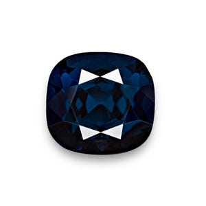 May include: A deep blue gemstone with a cushion cut. The gemstone has a high polish and is faceted.
