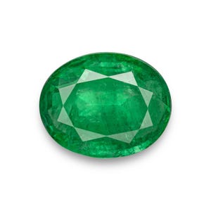 Peut inclure: Une pierre précieuse émeraude de forme ovale, d'un vert vif. La gemme présente de multiples facettes qui réfléchissent la lumière, créant un effet scintillant. La pierre est posée sur un fond blanc.