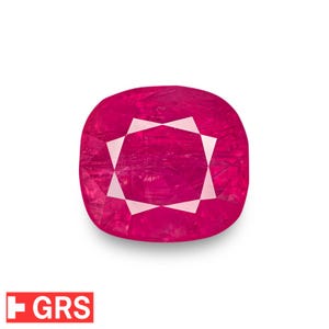 May include: A vibrant, cushion-cut ruby gemstone with a deep red hue. The gem features a starburst pattern of white facets at its center, creating a striking contrast. The GRS logo is visible in the lower left corner.