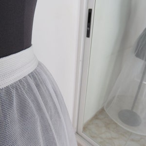 May include: A white tulle petticoat with a white elastic waistband. The petticoat is on a dress form and is shown from the front.