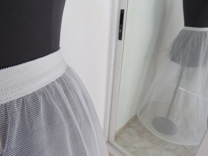 May include: A white tulle petticoat with a white elastic waistband. The petticoat is on a dress form and is shown from the front.