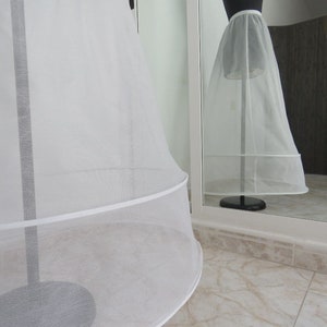 May include: A white tulle petticoat with a single layer of ruffles at the bottom. The petticoat is on a stand and is being displayed in a mirror.