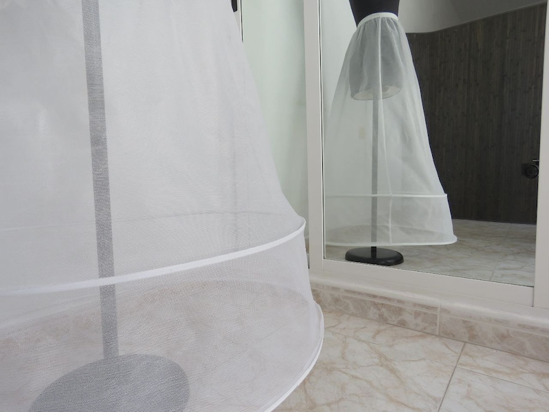 May include: A white tulle petticoat with a single layer of ruffles at the bottom. The petticoat is on a stand and is being displayed in a mirror.