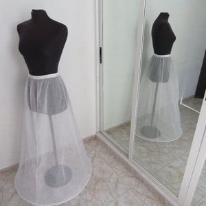 May include: A white tulle petticoat with a satin waistband. The petticoat is on a dress form in front of a mirror.
