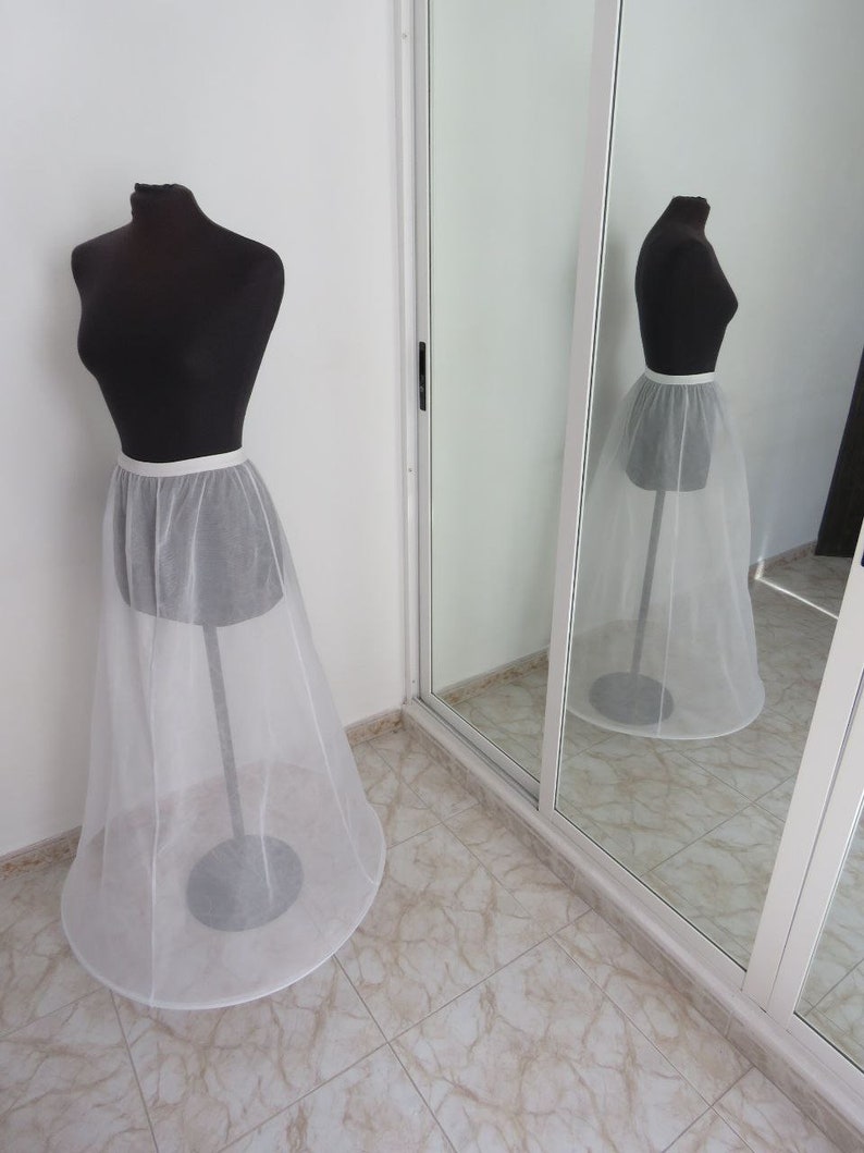 May include: A white tulle petticoat with a satin waistband. The petticoat is on a dress form in front of a mirror.