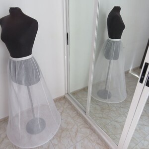 May include: A white tulle petticoat with a satin waistband on a dress form. The petticoat is a full circle shape and is designed to add volume to a skirt.