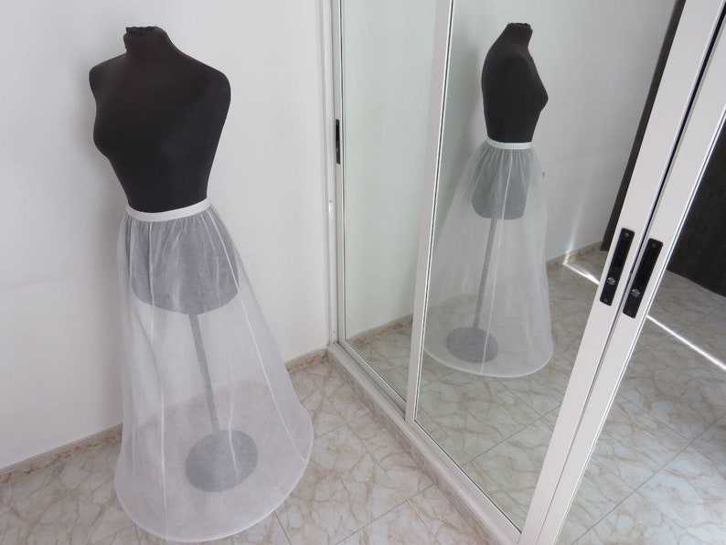 May include: A white tulle petticoat with a satin waistband on a dress form. The petticoat is a full circle shape and is designed to add volume to a skirt.