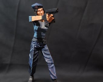May include: A low-poly style figurine of a police officer in a blue uniform and cap, holding a black handgun with both hands. The figure stands on a round black base with the red text RESIDENT EVIL printed on the front edge of the base.