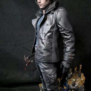 May include: A detailed figurine of a man in a black leather jacket with a fur collar, black gloves, and cargo pants. He holds a bloody weapon. The figure stands on a rocky base with a blue and yellow emblem.