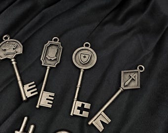 May include: Five antique-style metal keys with distinct head designs, including a shield, a sword, and a cross. Each key features a long shaft and a unique bit pattern at the bottom. The keys have a weathered, dark silver finish and a small loop at the top.